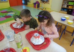 Dwójka dzieci maluje makietę wulkanu farbami.